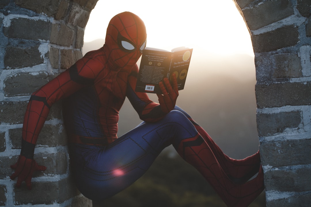 Person dressed as Spiderman, sitting in an arched brick window, reading a book.